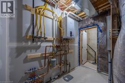 Utility area featuring a wall-mounted tankless water heater, exposed copper and yellow gas lines, visible electrical conduits, unfinished drywall, and a concrete floor -