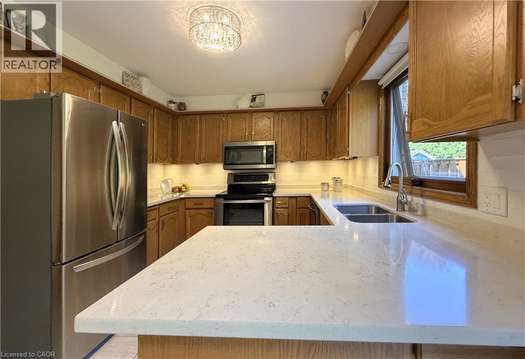 U-shaped kitchen featuring wood cabinetry, quartz countertops, and a white subway tile backsplash. - 7 Mann Avenue, Simcoe, ON - Indoor Photo Showing Kitchen With Stainless Steel Kitchen With Double Sink