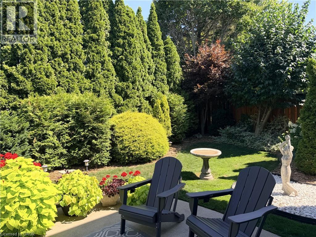 Beautifully landscaped backyard with towering trees forming a back hedge, mature gardens with perennials, and a concrete patio. - 7 Mann Avenue, Simcoe, ON - Outdoor With Deck Patio Veranda