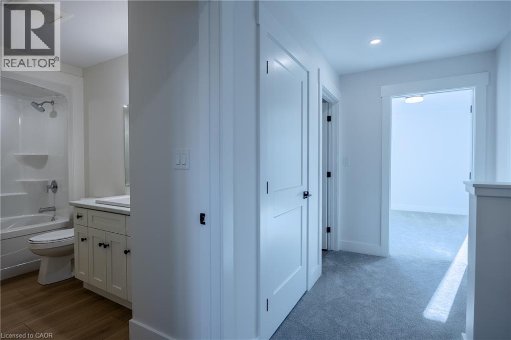 Bathroom featuring a white vanity with a rectangular undermount sink, a white countertop, wood-finish flooring, a white toilet, and a white tub with shower - 107 Amber Street, Waterford, ON - Indoor Photo Showing Bathroom