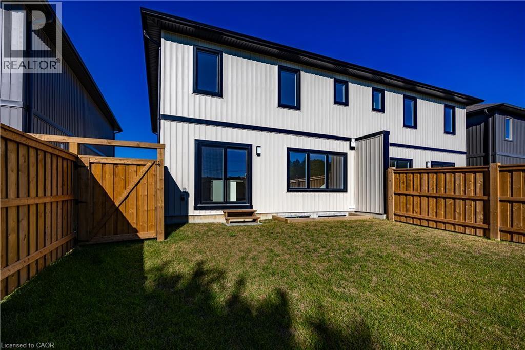 Expansive grassy yard with a wooden privacy fence, featuring a contemporary white siding exterior with contrasting black trim - 107 Amber Street, Waterford, ON - Outdoor