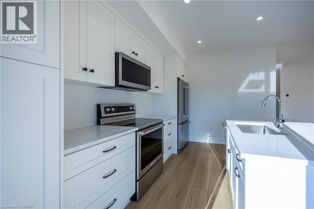 Modern kitchen featuring white shaker cabinetry, stainless steel appliances, light wood-finish flooring, recessed lighting, and an island with an undermount sink - 107 Amber Street, Waterford, ON - Indoor Photo Showing Kitchen With Upgraded Kitchen