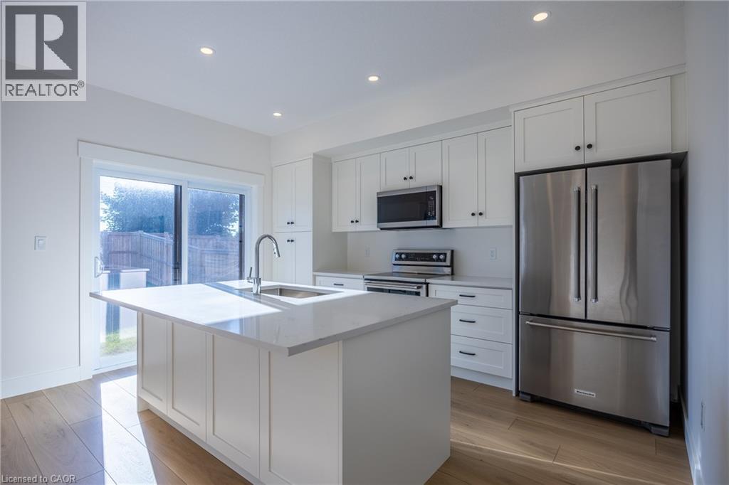 Modern kitchen featuring white shaker cabinetry, stainless steel appliances, a center island with an undermount sink, recessed lighting, and wood-finish flooring - 107 Amber Street, Waterford, ON - Indoor Photo Showing Kitchen
