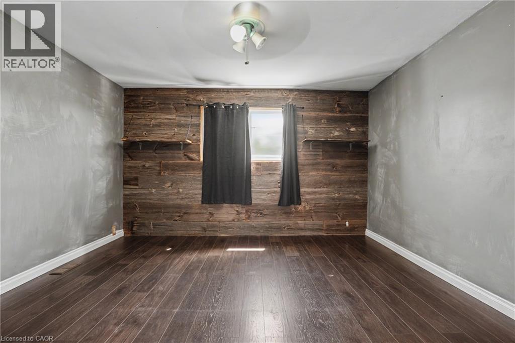 Room featuring wood-finish flooring, a rustic wood accent wall with integrated shelving, and light gray painted walls - 485 Cochrane Road, Hamilton, ON - Indoor Photo Showing Other Room
