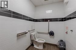 Restroom featuring white rectangular wall tiles with a black accent band, wood-finish flooring, and stainless steel grab bars -