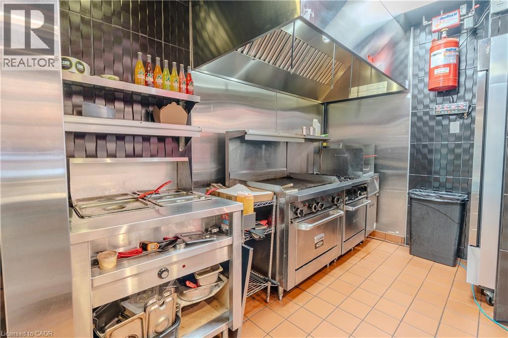 Commercial kitchen featuring stainless steel appliances, a large exhaust hood, tile flooring, and dark textured wall tiling - 96 Gerrard St E, Toronto, ON