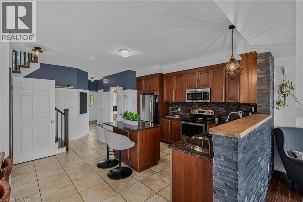 Kitchen with stone veneer accent wall, wood cabinetry, and stainless steel appliances - 174 Woodway Trail, Simcoe, ON - Indoor Photo Showing Kitchen