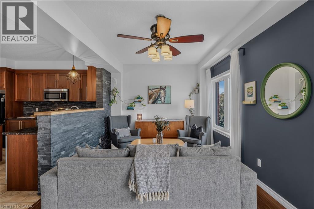 Open-concept living space featuring a stone-clad half-wall, wood-finish flooring, a ceiling fan with integrated lighting, and a kitchen with warm wood cabinetry and stainless steel appliances - 174 Woodway Trail, Simcoe, ON - Indoor With Fireplace
