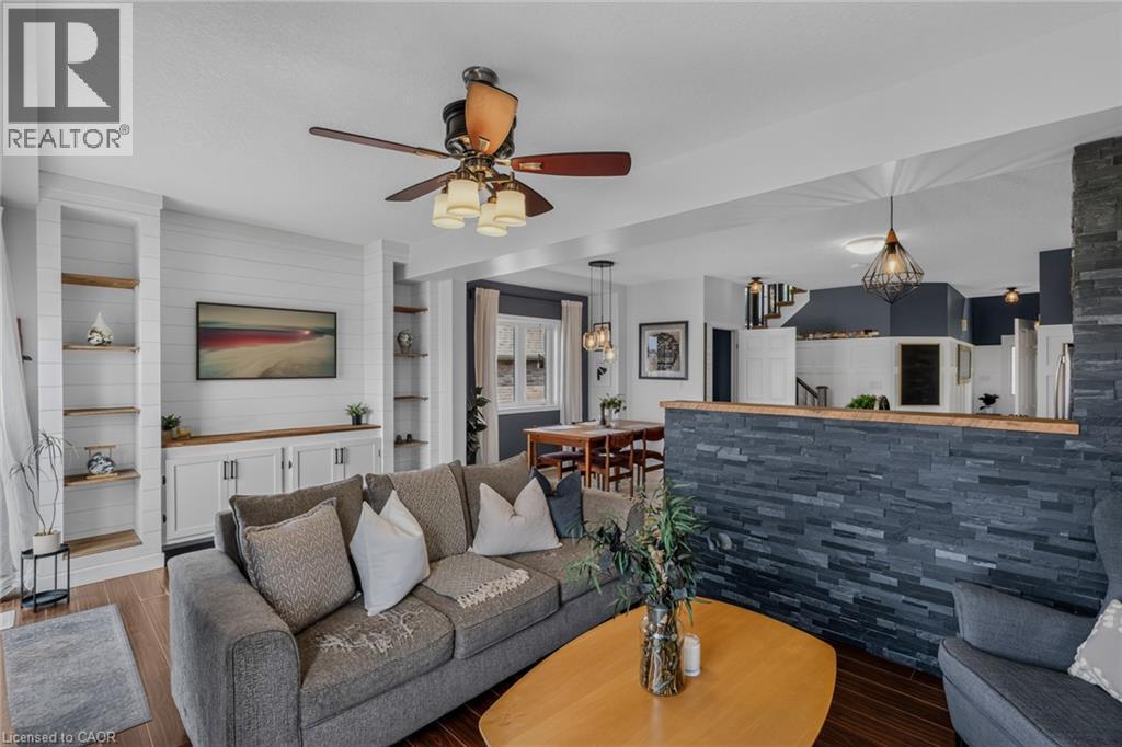 Living area featuring dark wood-finish flooring, a built-in entertainment center with shiplap backing, integrated shelving, and a ceiling fan - 174 Woodway Trail, Simcoe, ON - Indoor Photo Showing Living Room