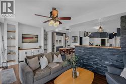 Living area featuring dark wood-finish flooring, a built-in entertainment center with shiplap backing, integrated shelving, and a ceiling fan -