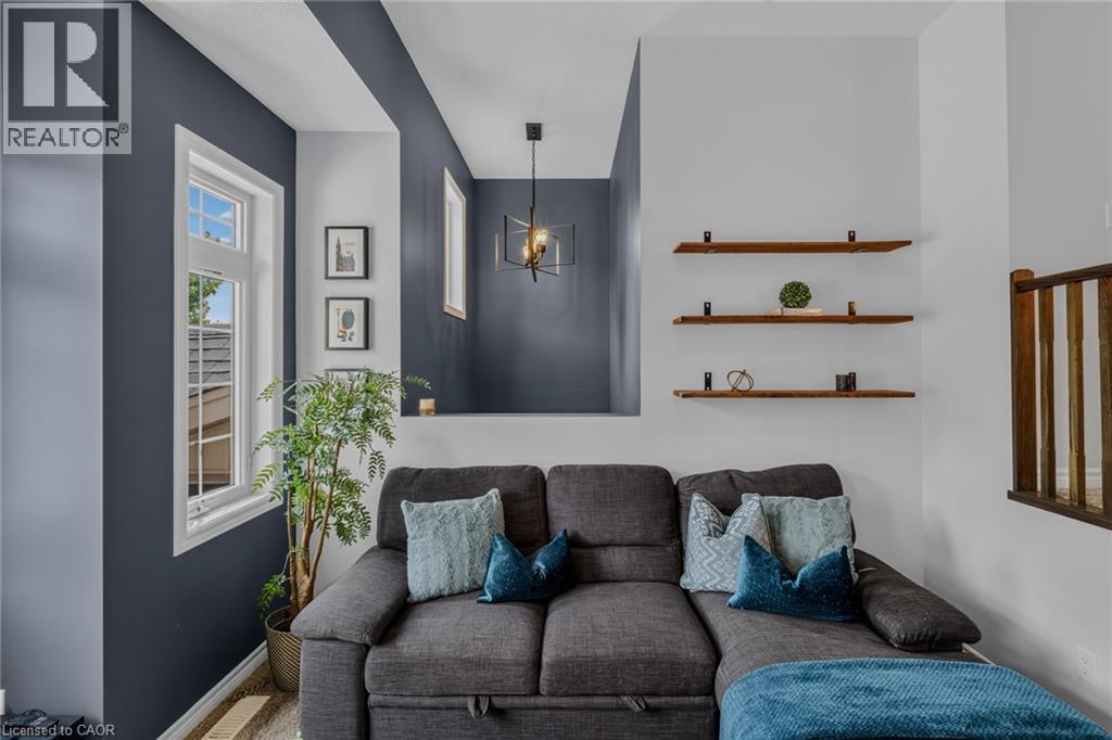 Living area featuring a distinct accent wall, multiple windows with white trim, a decorative pendant light fixture, and three wall-mounted wood-finish shelves - 174 Woodway Trail, Simcoe, ON - Photo Showing Living Room