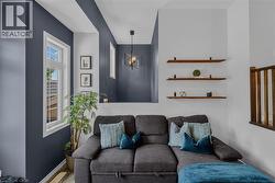 Living area featuring a distinct accent wall, multiple windows with white trim, a decorative pendant light fixture, and three wall-mounted wood-finish shelves -