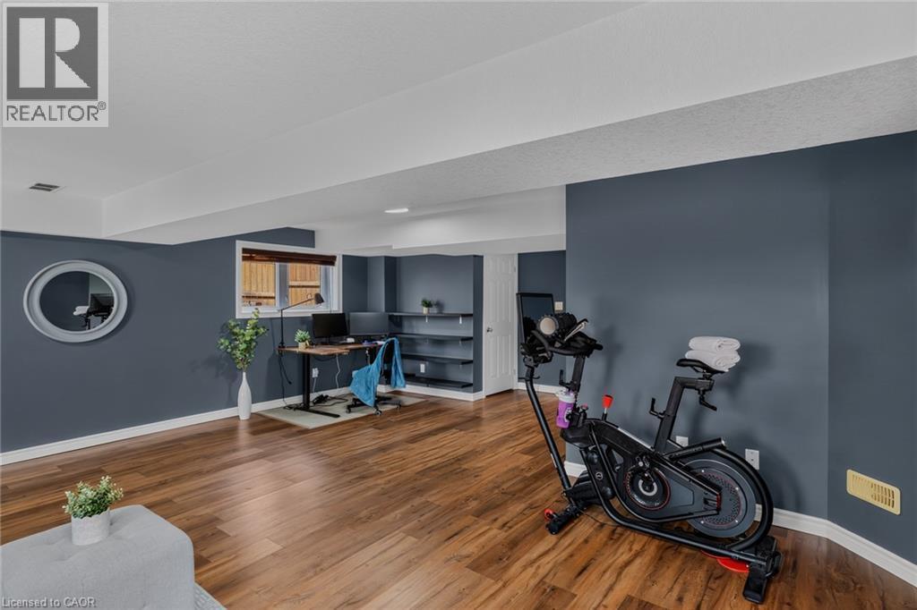 Spacious lower-level room featuring wood-finish flooring, recessed lighting, a window with horizontal blinds, and built-in shelving - 174 Woodway Trail, Simcoe, ON - Indoor Photo Showing Other Room