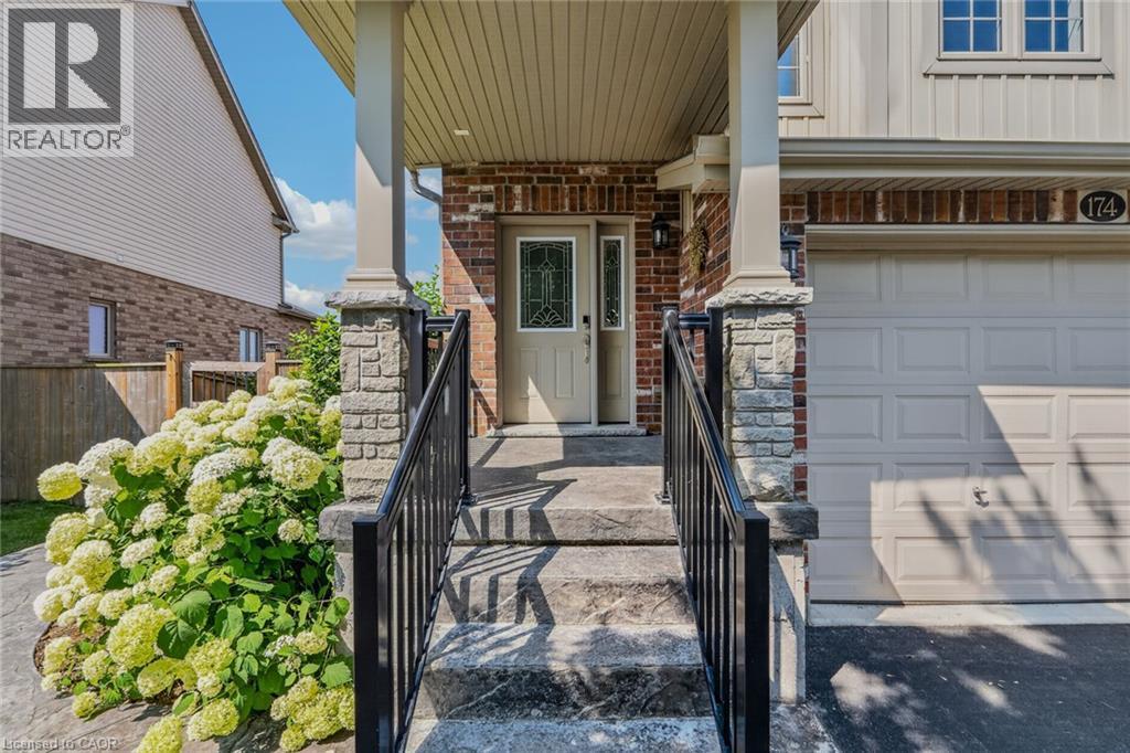 Brick and siding exterior featuring a covered porch, stone-clad columns, and a paneled garage door - 174 Woodway Trail, Simcoe, ON - Outdoor