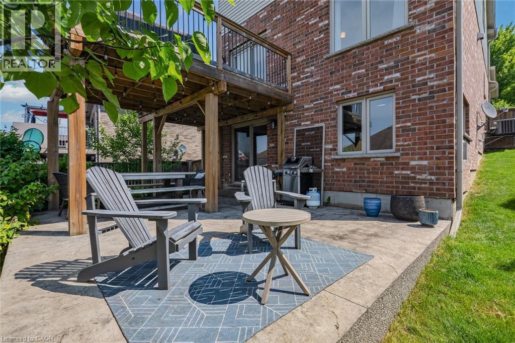 Lower-level patio featuring stamped concrete, a grassed area, and a covered wooden deck structure - 174 Woodway Trail, Simcoe, ON - Outdoor With Deck Patio Veranda