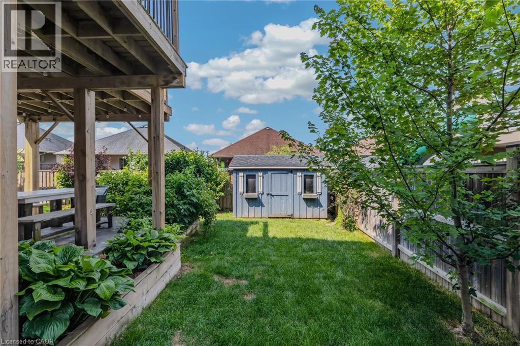 Rear yard featuring a wood deck with an overhead balcony, a wood garden bed, a freestanding storage shed, and a wooden privacy fence - 174 Woodway Trail, Simcoe, ON - Outdoor