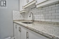 Kitchen area featuring white cabinetry with brushed nickel hardware, a stainless steel sink with a high-arc faucet, and light-toned speckled countertops -