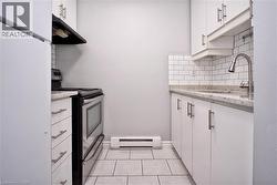 Kitchen featuring white cabinetry with brushed nickel hardware, speckled countertops, subway tile backsplash, and stainless steel appliances -