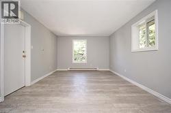 Spacious room featuring light grey walls, wood-finish flooring, white trim, and two windows providing natural light -