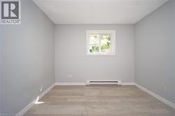 Neutral-toned room featuring a window with white trim, light wood-finish flooring, and white baseboards -