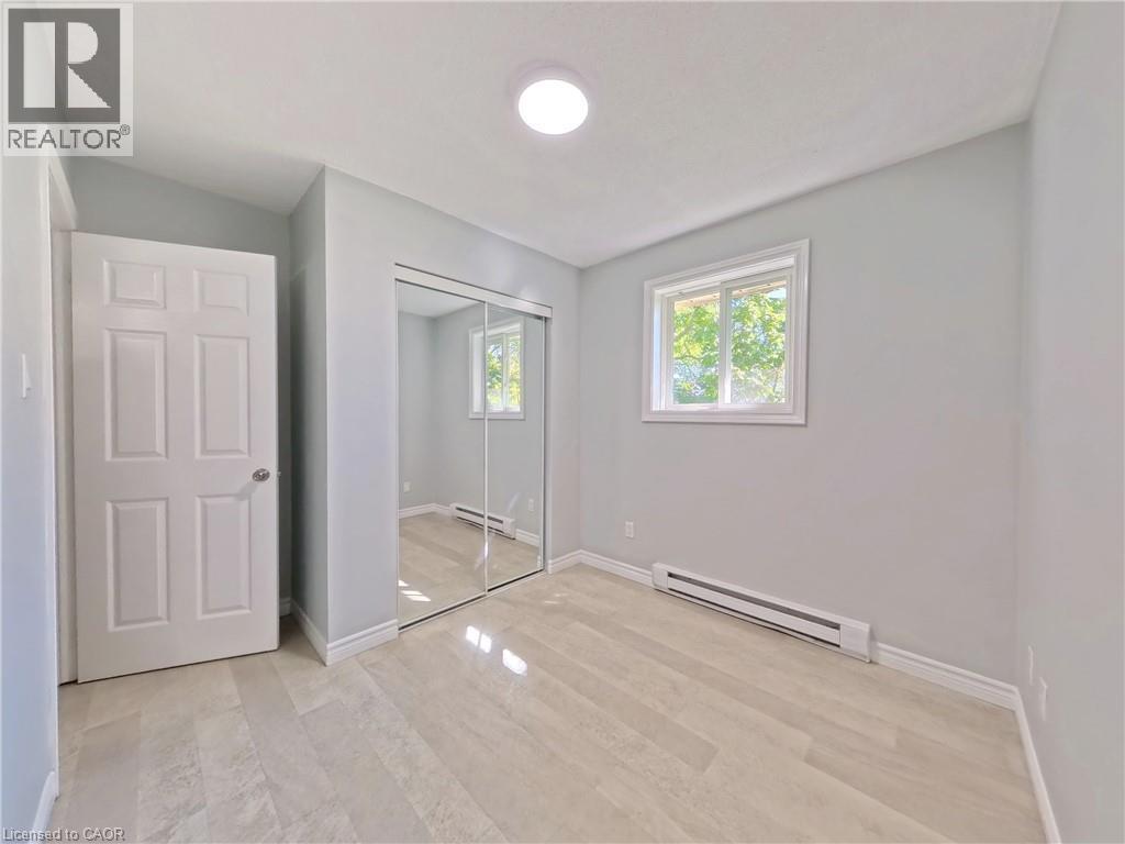 Bedroom featuring light grey walls, light wood-finish flooring, a contemporary ceiling light fixture, and a window with white trim - 119 Cedar Street S Unit# 14, Kitchener, ON - Indoor Photo Showing Other Room