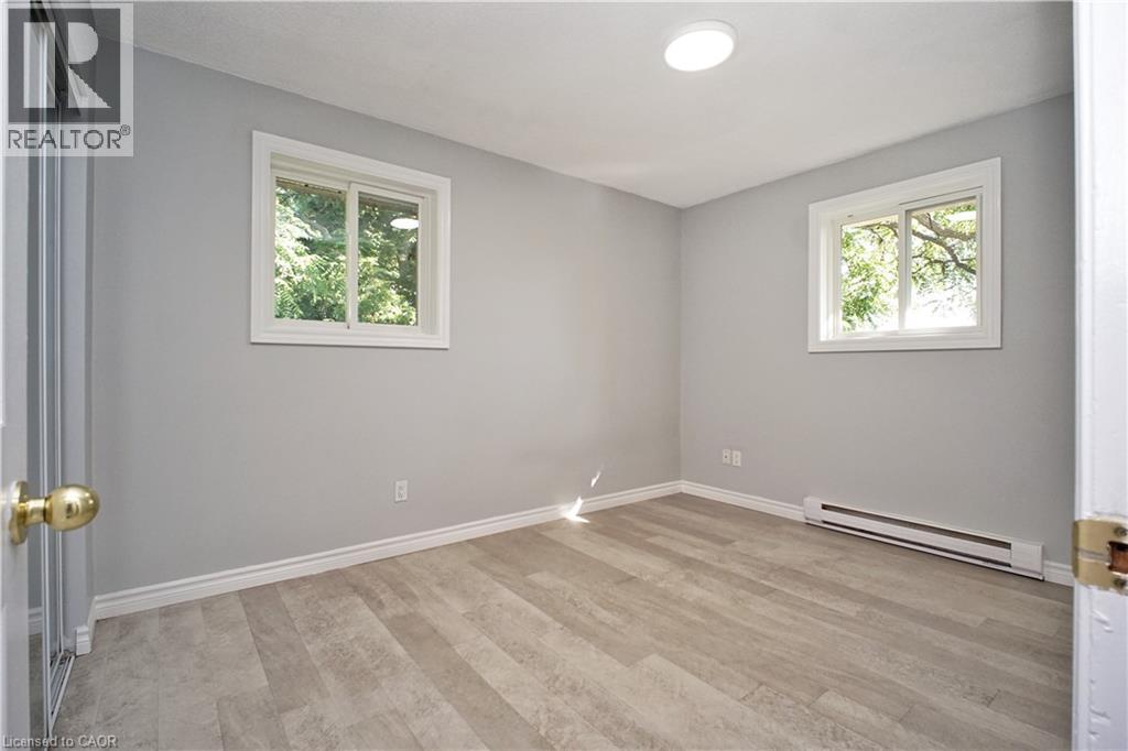 Room featuring neutral gray walls, wood-finish flooring, two windows with white trim, and a ceiling-mounted light fixture - 119 Cedar Street S Unit# 14, Kitchener, ON - Indoor Photo Showing Other Room