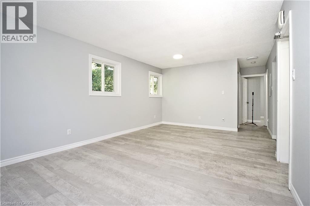 Spacious room featuring light gray walls, wood-finish flooring, two windows with white trim, and a ceiling-mounted light fixture - 119 Cedar Street S Unit# 14, Kitchener, ON - Indoor Photo Showing Other Room