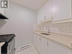 Kitchen featuring white cabinetry, subway tile backsplash, speckled countertops, stainless steel sink with gooseneck faucet, and tile flooring -