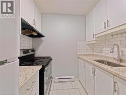 Contemporary kitchen featuring white cabinetry, subway tile backsplash, granite-finish countertops, stainless steel sink with a pull-down faucet, and a black range with an overhead hood -
