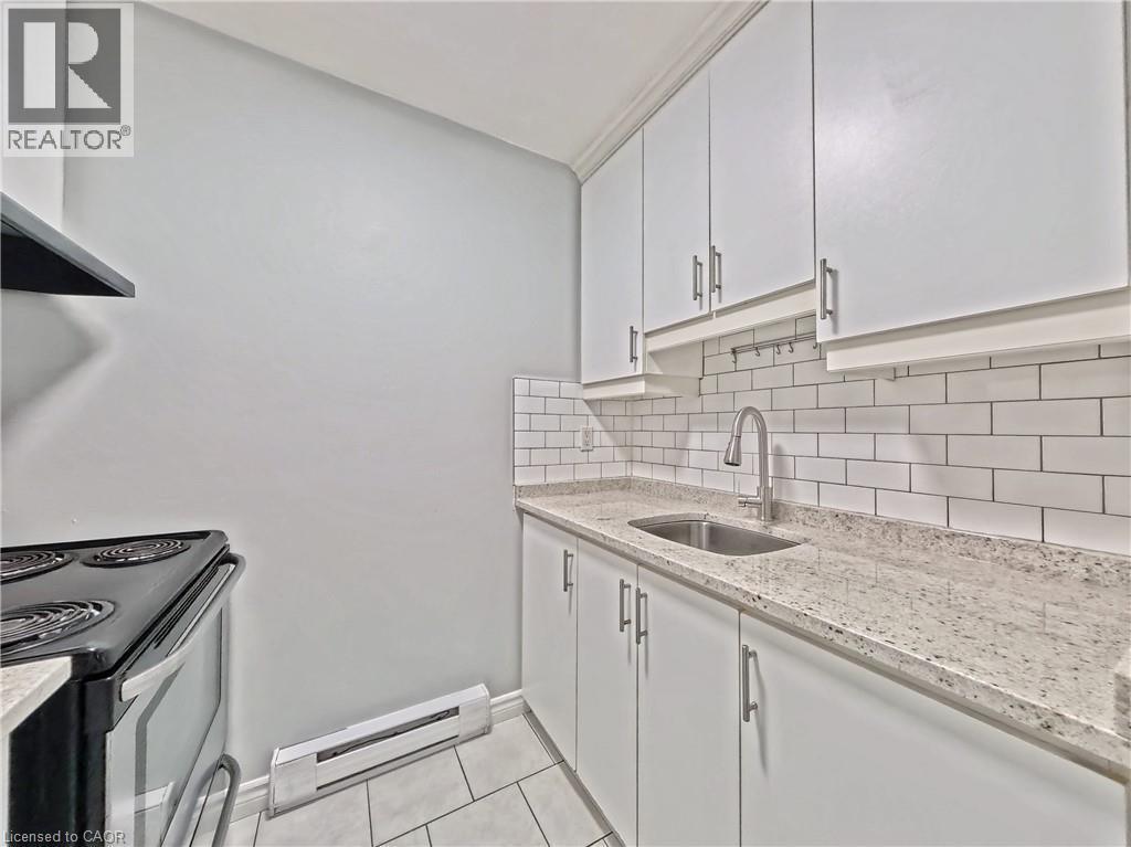 Kitchen featuring white shaker-style cabinetry, a stainless steel sink with a gooseneck faucet, light-toned speckled countertops, and a white subway tile backsplash - 119 Cedar Street S Unit# 14, Kitchener, ON - Indoor Photo Showing Kitchen