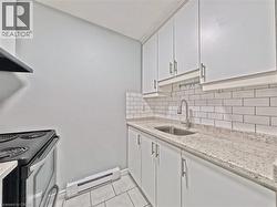 Kitchen featuring white shaker-style cabinetry, a stainless steel sink with a gooseneck faucet, light-toned speckled countertops, and a white subway tile backsplash -