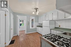 Kitchen featuring extensive white cabinetry, a white refrigerator, a gas range, a stainless steel sink, and wood-finish flooring -