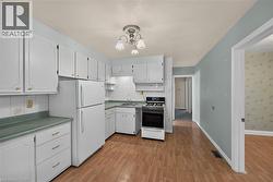 Kitchen featuring white cabinetry, wood-finish flooring, white appliances, light blue walls, and a tiled backsplash -