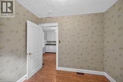 Interior room featuring wood-finish flooring, patterned wallpaper, and white baseboards -