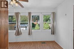 Room featuring three windows with exterior views, wood-finish flooring, and a ceiling fan with integrated lighting -