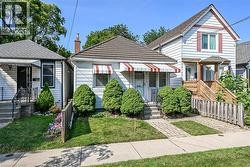 White siding exterior with a shingled roof, featuring a front porch with a striped awning -