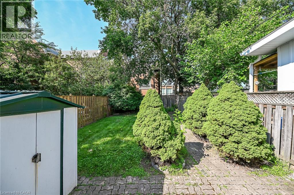 Landscaped backyard featuring a paver stone pathway, mature manicured evergreens, a wooden privacy fence, a storage shed, and a lush green lawn - 155 Newlands Avenue, Hamilton, ON - Outdoor