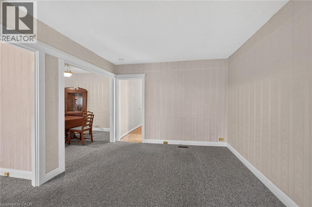 Carpeted room with patterned wall covering, baseboard trim, and a doorway leading to a room with wood-finish flooring - 155 Newlands Avenue, Hamilton, ON - Indoor Photo Showing Other Room