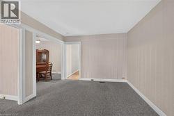 Carpeted room with patterned wall covering, baseboard trim, and a doorway leading to a room with wood-finish flooring -