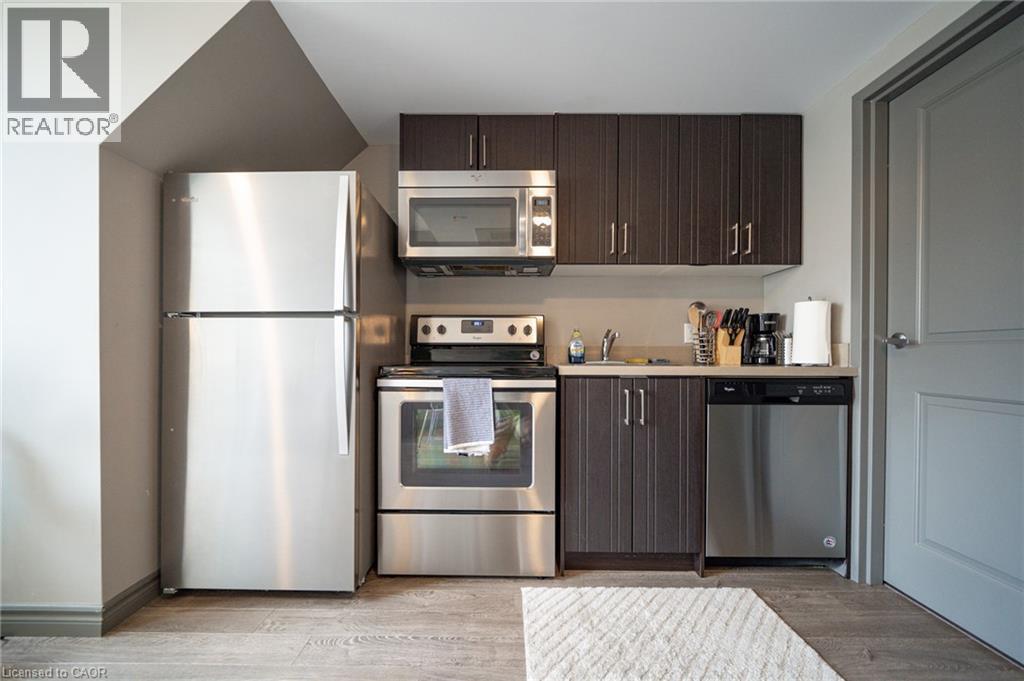 Compact kitchen featuring a full suite of stainless steel appliances, wood-finish flooring, dark wood cabinetry, and light-toned countertops - 321 Spruce Street Unit# 710, Waterloo, ON - Indoor Photo Showing Kitchen With Stainless Steel Kitchen