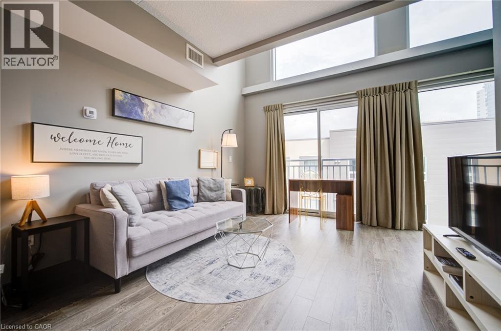 Living space featuring high ceilings, wood-finish flooring, a full wall of windows, and a glass sliding door opening to a balcony - 321 Spruce Street Unit# 710, Waterloo, ON - Indoor Photo Showing Living Room