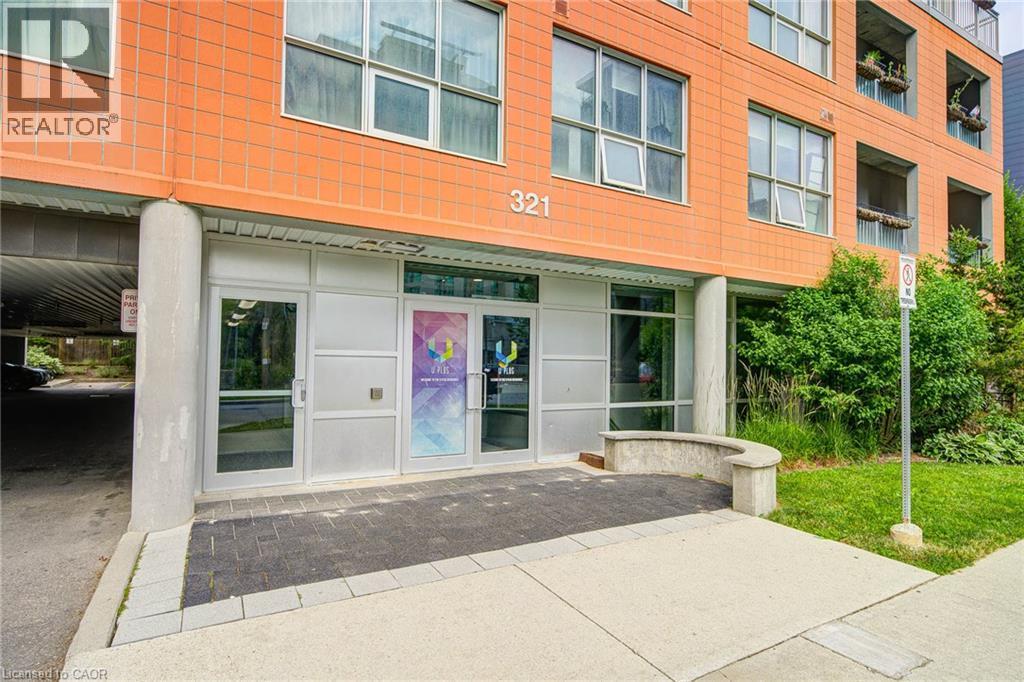 Exterior entrance featuring clear glass doors, a concrete walkway, and a landscaped area with mature shrubs - 321 Spruce Street Unit# 710, Waterloo, ON - Outdoor