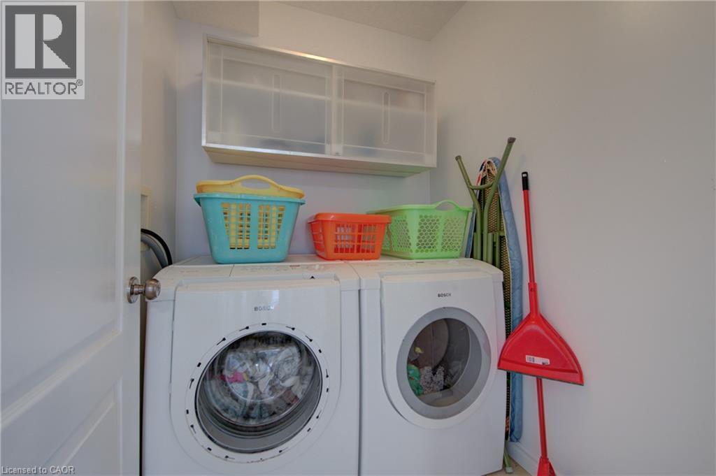 Dedicated laundry area featuring a front-loading washer and dryer, upper wall-mounted cabinetry, and a light-colored wall finish - 729 Keats Way, Waterloo, ON - Indoor Photo Showing Laundry Room