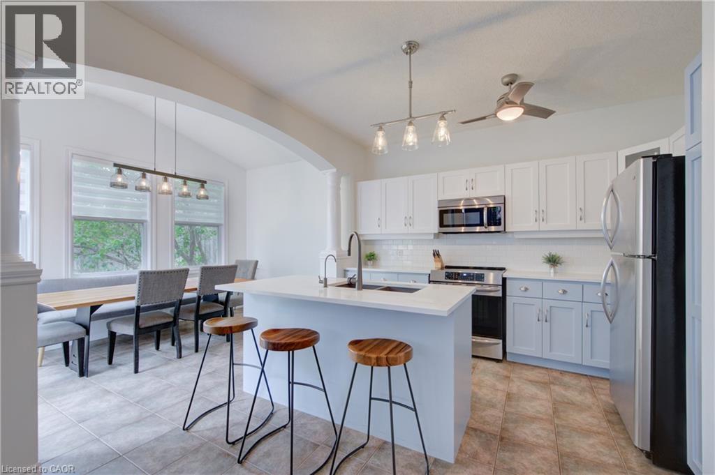Kitchen featuring white upper cabinetry, light blue lower cabinetry, stainless steel appliances, a white subway tile backsplash, and an island with a white countertop - 729 Keats Way, Waterloo, ON - Indoor Photo Showing Kitchen
