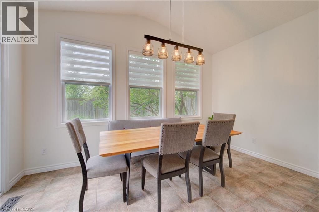 Dining area featuring a linear pendant light fixture with five glass shades, three windows with horizontal blinds, and tile flooring - 729 Keats Way, Waterloo, ON - Indoor Photo Showing Dining Room