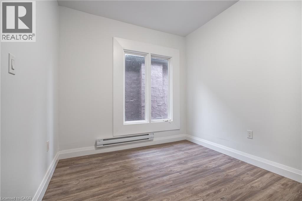 Room featuring wood-finish flooring, white walls, white baseboards, and a window with white trim - 524 King Street E Unit# 3, Hamilton, ON - Indoor Photo Showing Other Room