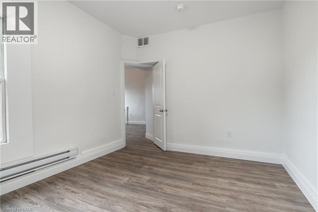 Room featuring wood-finish flooring, white painted walls, a window with a white frame, and white baseboards - 524 King Street E Unit# 3, Hamilton, ON - Indoor Photo Showing Other Room