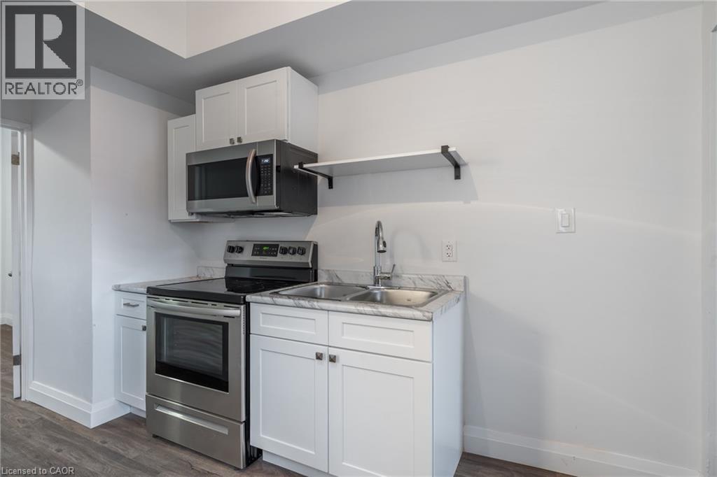 Compact kitchen featuring white cabinetry, stainless steel appliances, marble-look countertops, and wood-finish flooring - 524 King Street E Unit# 3, Hamilton, ON - Indoor Photo Showing Kitchen With Stainless Steel Kitchen With Double Sink