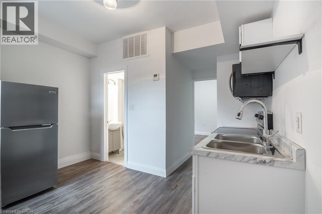 Compact kitchen featuring stainless steel appliances, wood-finish flooring, white cabinetry, a dual basin sink, and a countertop with a marble-style finish - 524 King Street E Unit# 3, Hamilton, ON - Indoor Photo Showing Kitchen With Double Sink