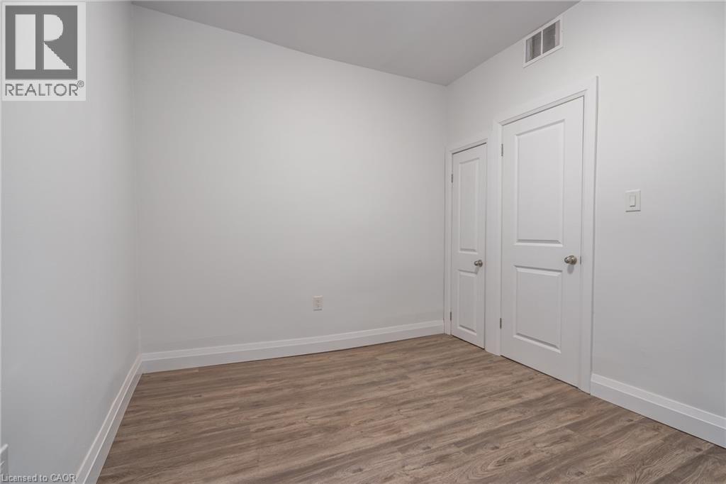 Neutral white walls featuring wood-finish flooring, white baseboards, and two paneled interior doors with silver-tone hardware - 524 King Street E Unit# 3, Hamilton, ON - Indoor Photo Showing Other Room